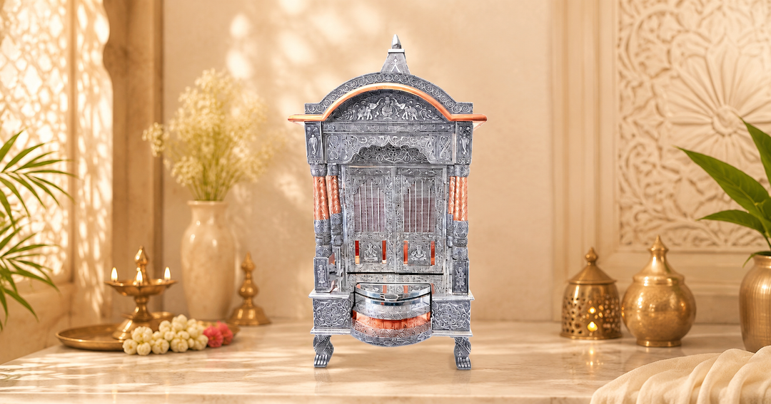 Ornate silver and copper pooja mandir placed on a marble surface with warm beige decor, brass lamps, floral accents, and soft natural light in the background.